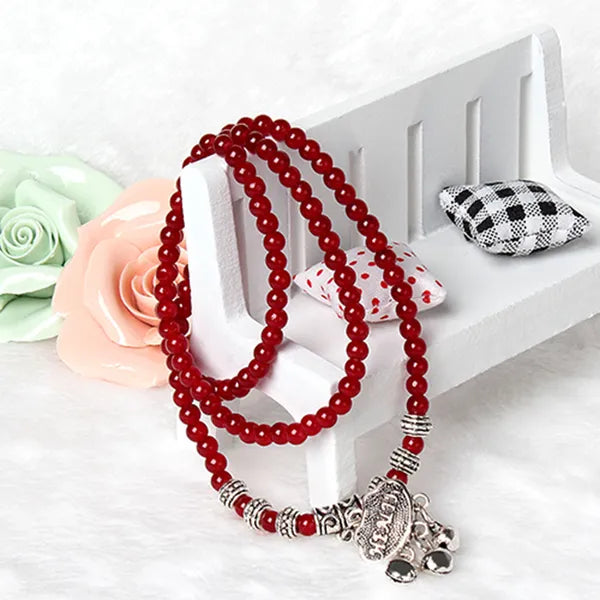 Red beaded necklace with silver charms on a white surface with decorative pillows and flowers.