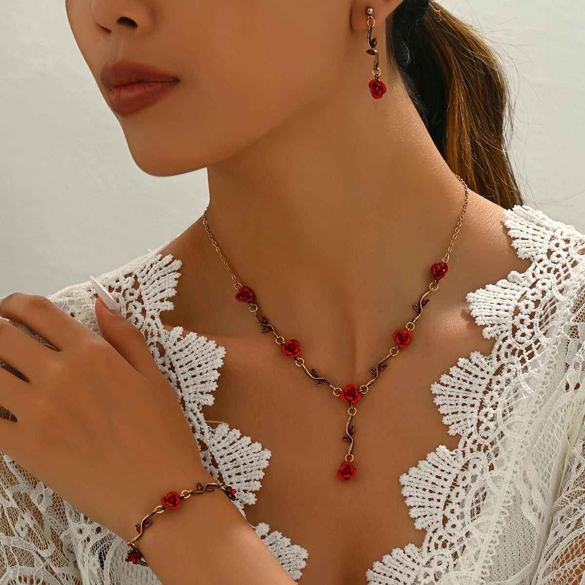 Woman wearing a gold necklace with red floral pendants and matching bracelet.