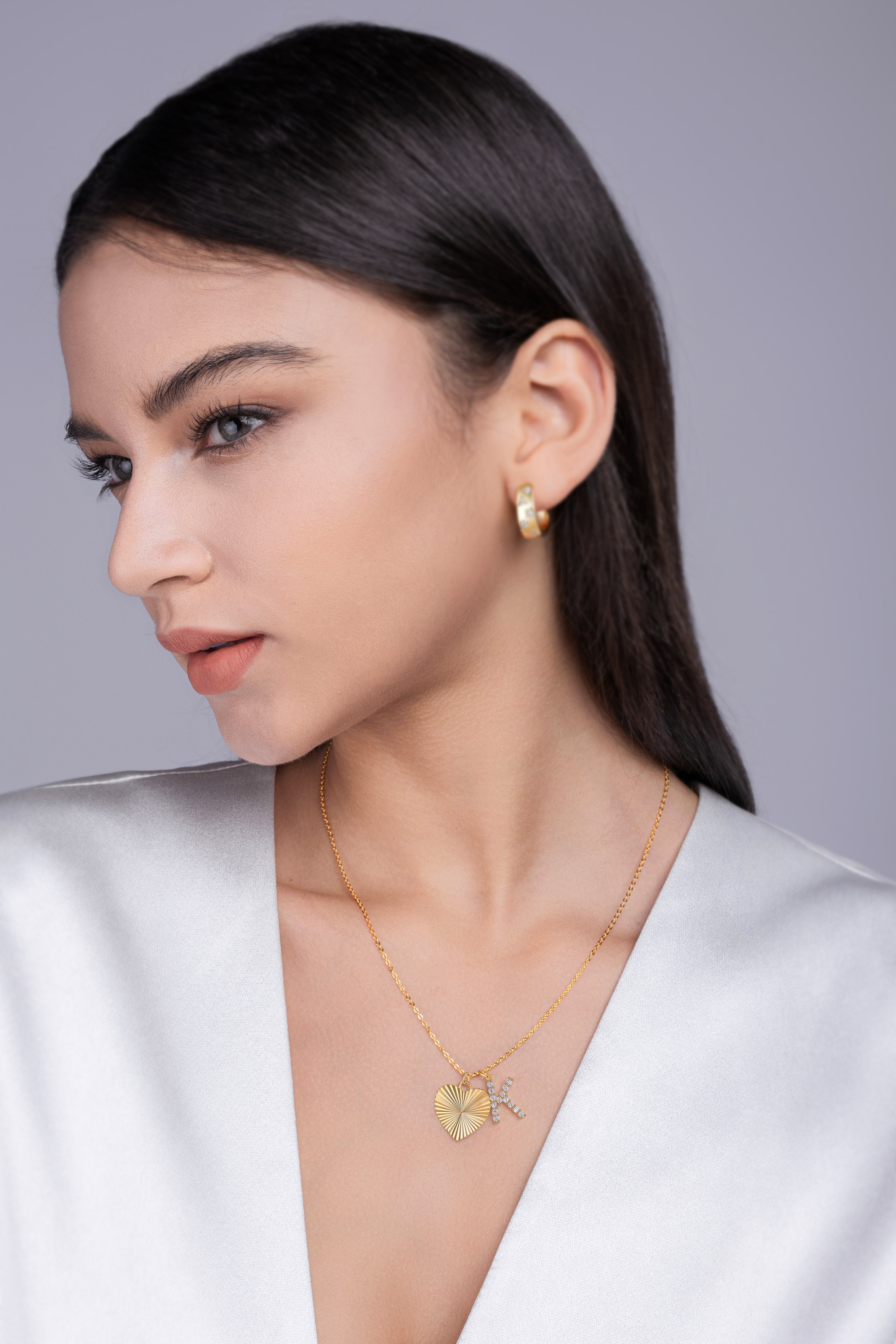 Woman wearing gold jewelry including earrings and a necklace against a gray background