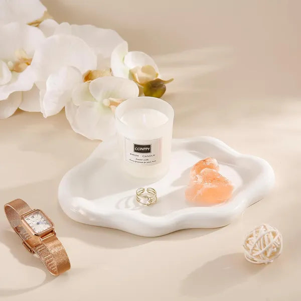 Candle, jewelry, and decorative items on a white surface with flowers in the background
