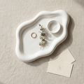 White ceramic dish with a ring and dried plant on a beige surface