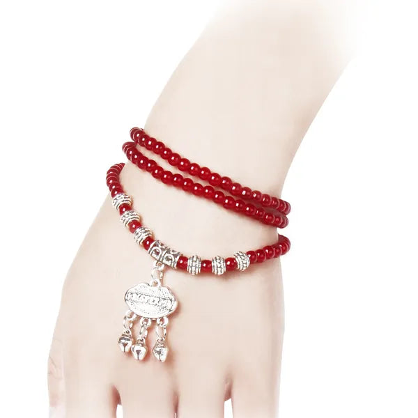 Red beaded bracelet with a silver charm on a wrist against a white background